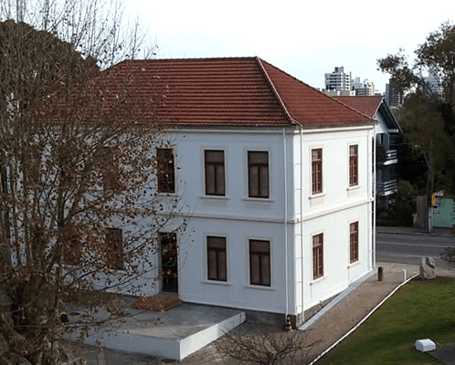Foto da parte traseira do Museu do Imigrante. Prédio com várias janelas e uma árvore na frente em parte da parede