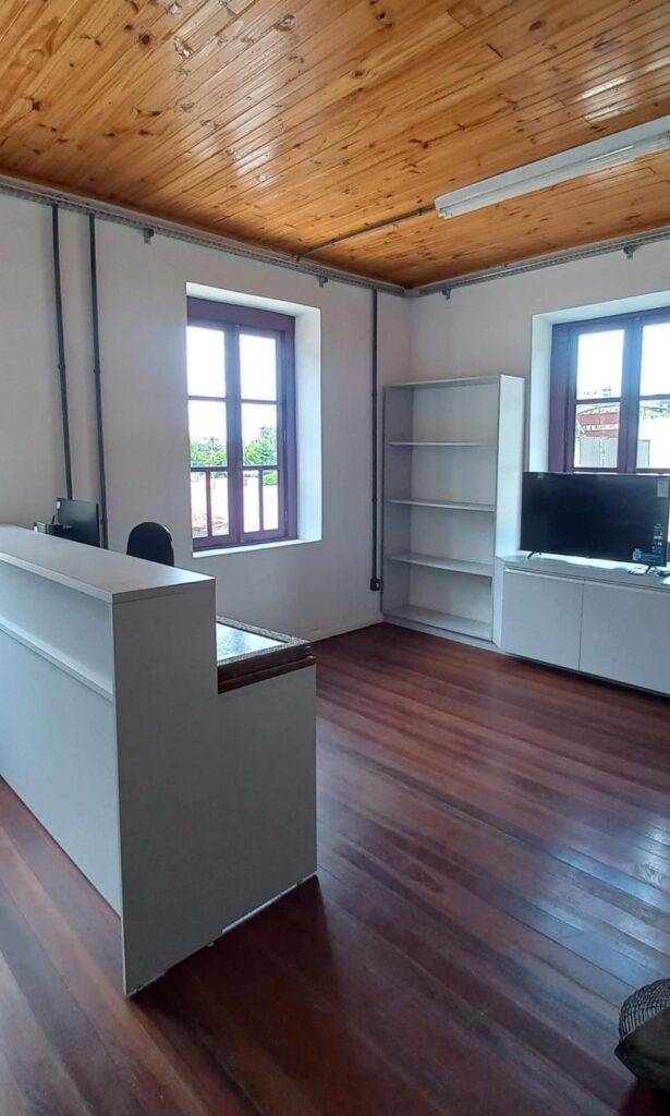 Foto da recepção do Centro Cultural Tuiuty mostrando uma bancada e estantes. Ao fundo, janelas.