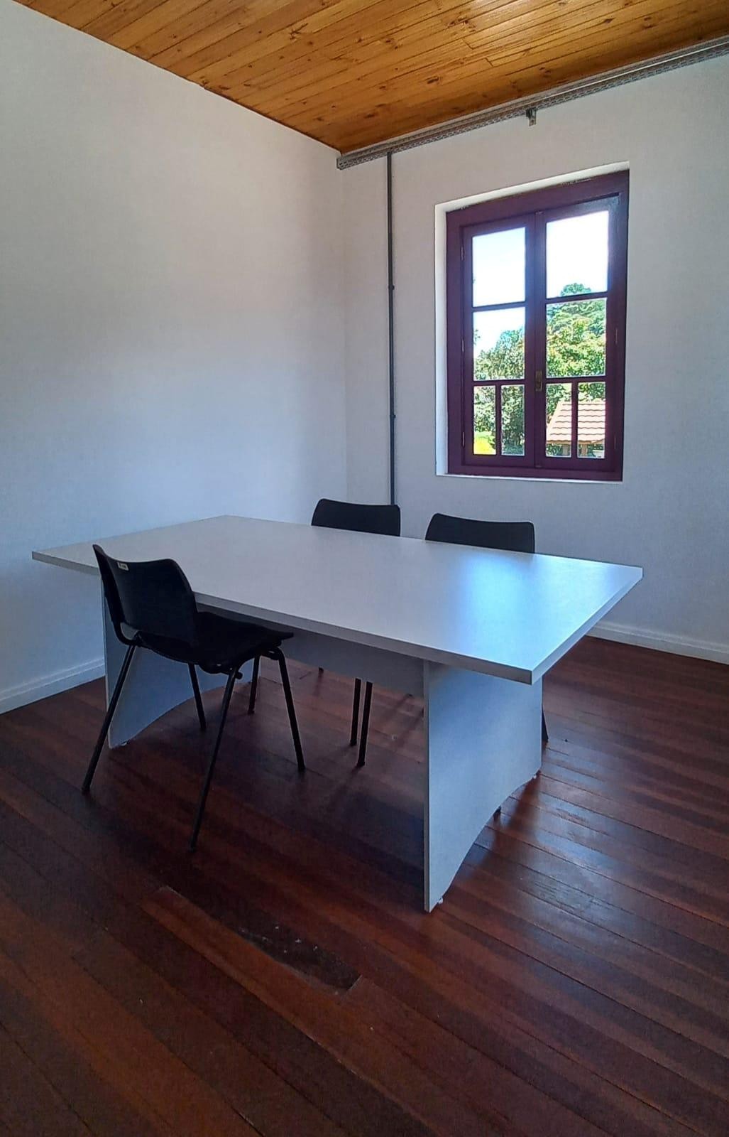 Sala contendo uma mesa e cadeiras ao seu redor. Ao fundo, uma janela