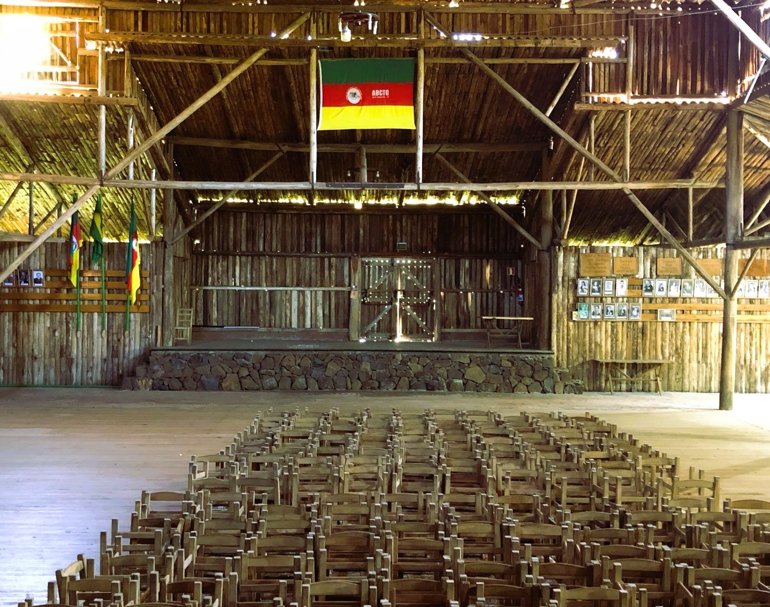 Parte interna do galpão mostrando palco e diversas cadeiras em frente a ele