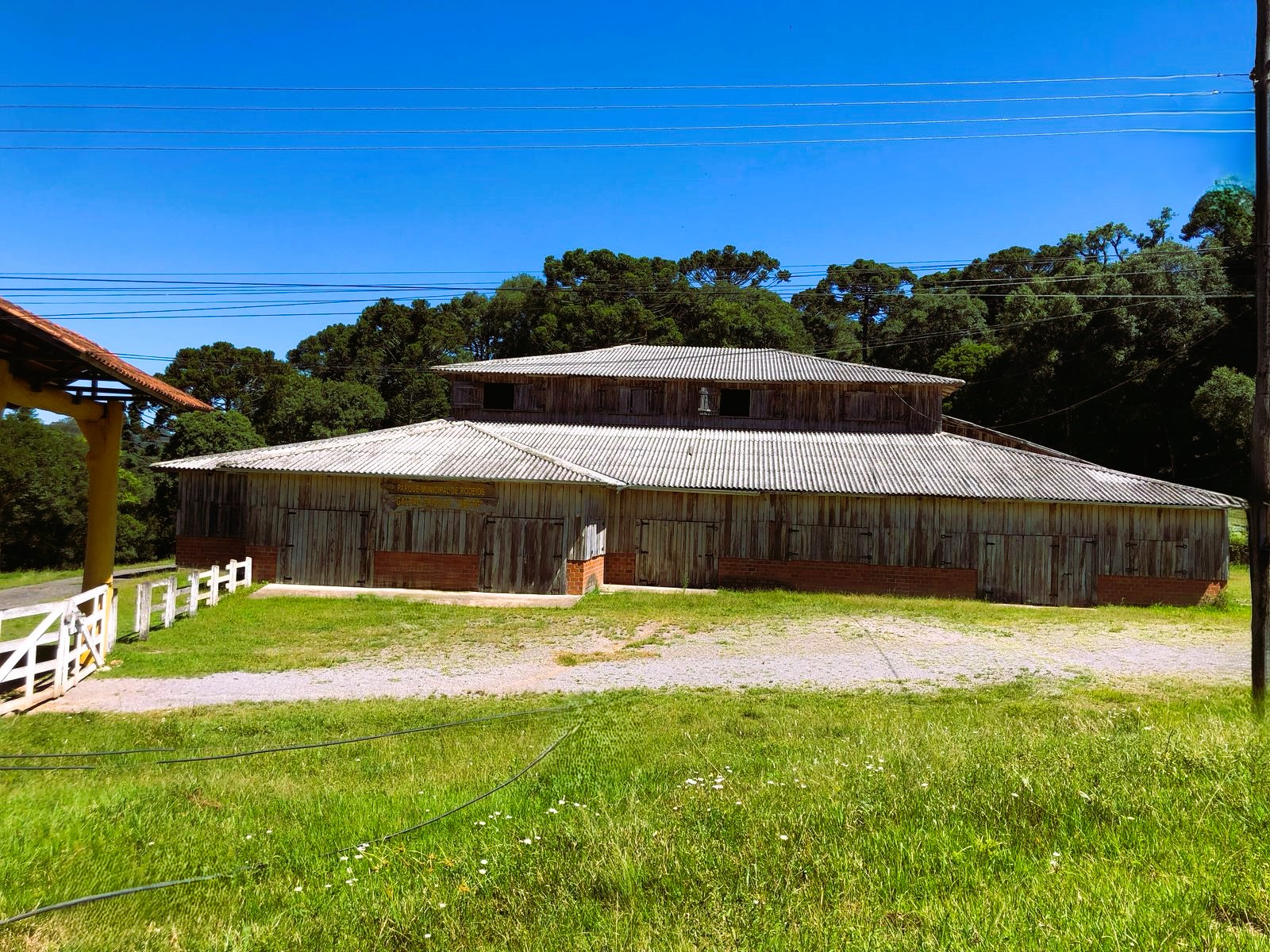Galpão de madeira e árvores ao fundo.